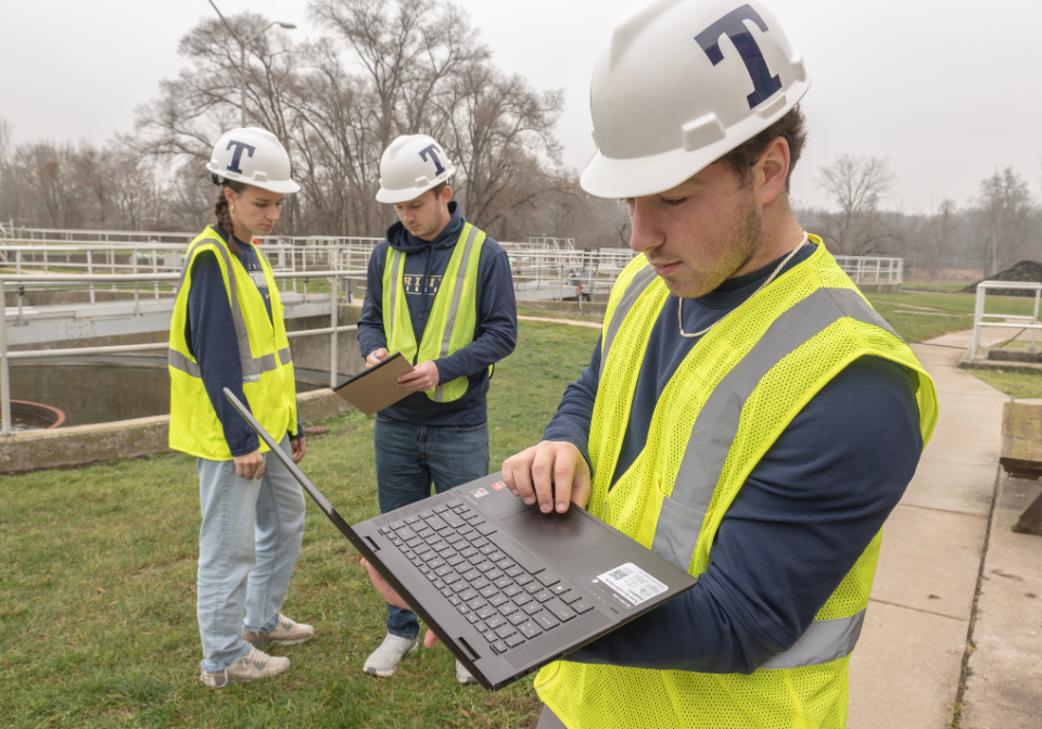 three trine students in safety vests check surveying results at a wastewater treatment plant