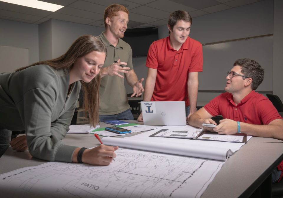 four students discuss around a blueprint