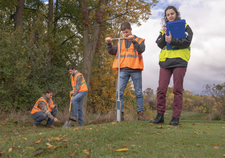 four students in safety vests collect soil samples on trine's zollner golf course