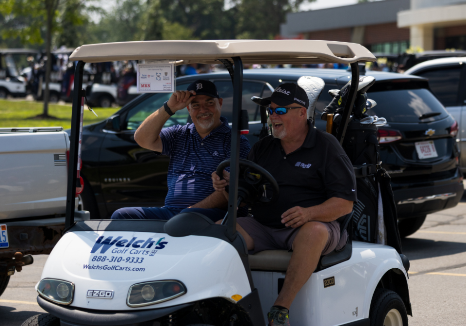 men on a golf cart heading to the course for the scholarship golf outing