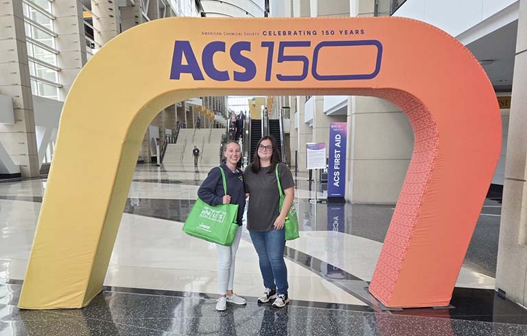 Two female students under ACS 150 arch
