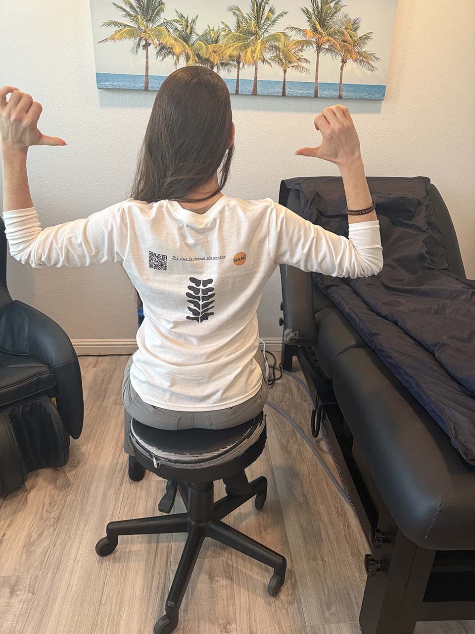 Angela Kesler Santoro seated pointing to back of shirt.