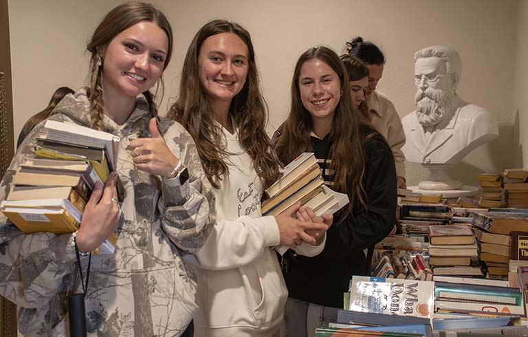 Students smiling at camera; two of them have armloads of books