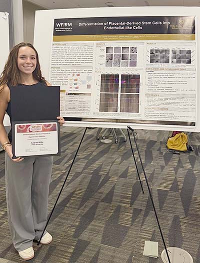 Female student holding certificate and standing in front of research poster