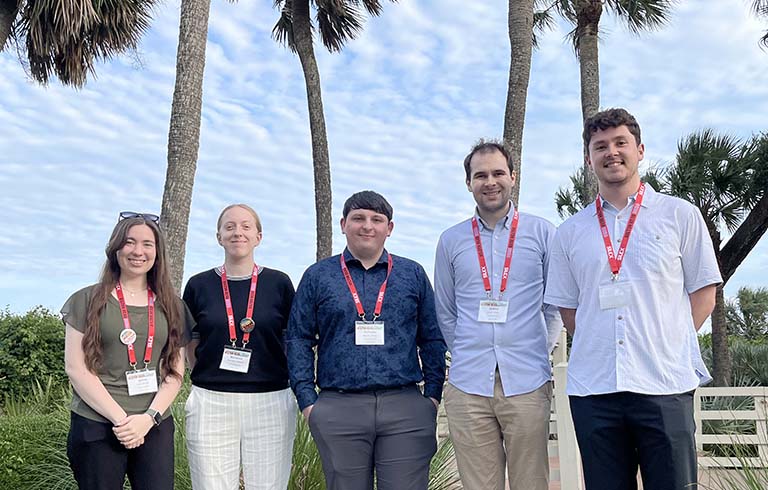 Four students and one faculty member standing in front of palm trees