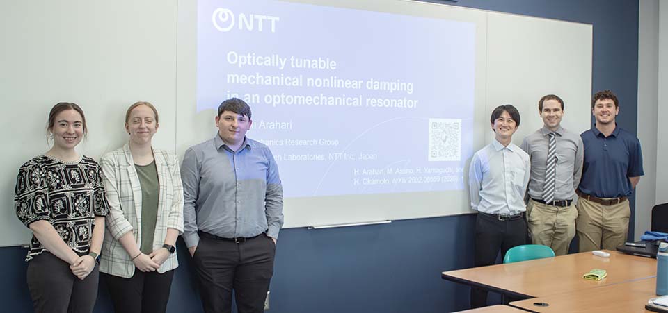 Four students, one faculty and visiting lecturer in front of screen