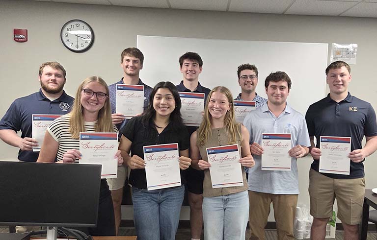Nine students holding certificates stating they are certified to prepare taxes at VITA site