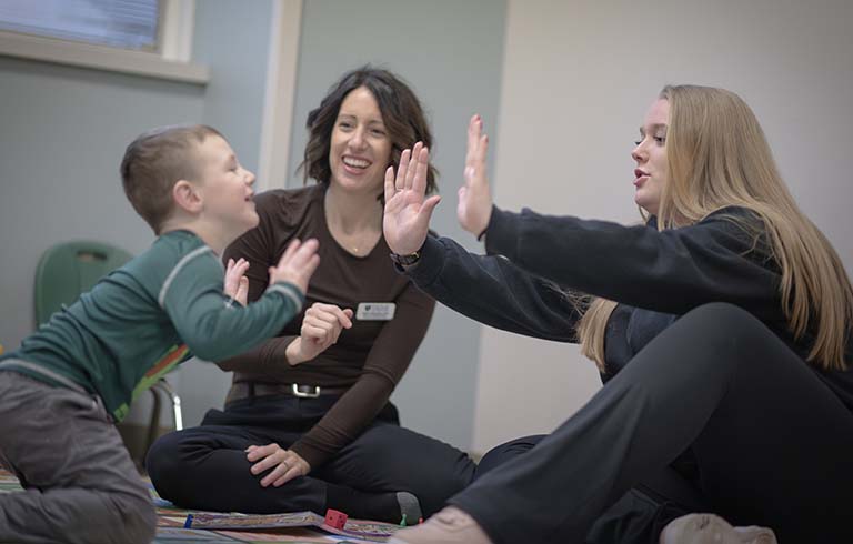 Child and student playing patty-cake with occupational therapy faculty member supervising
