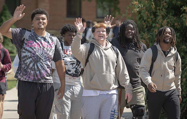 Students waving as they walk across campus